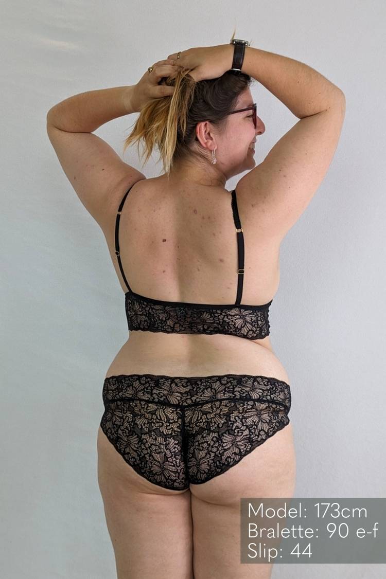 Donna in lingerie di pizzo nero tiene i capelli raccolti.