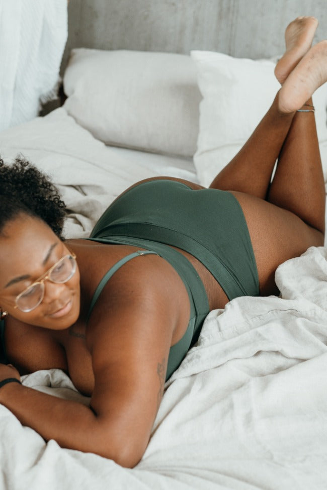 Modèle en lingerie verte allongé sur le lit, l'accent est mis sur le fin Slip.