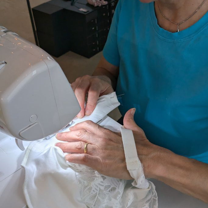Die Frau näht an einer Nähmaschine ihr eigenes Bralette aus Spitze und Tencel in weiss