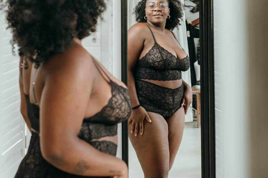 Person in fine lace underwear in black looks at herself in a double mirror,