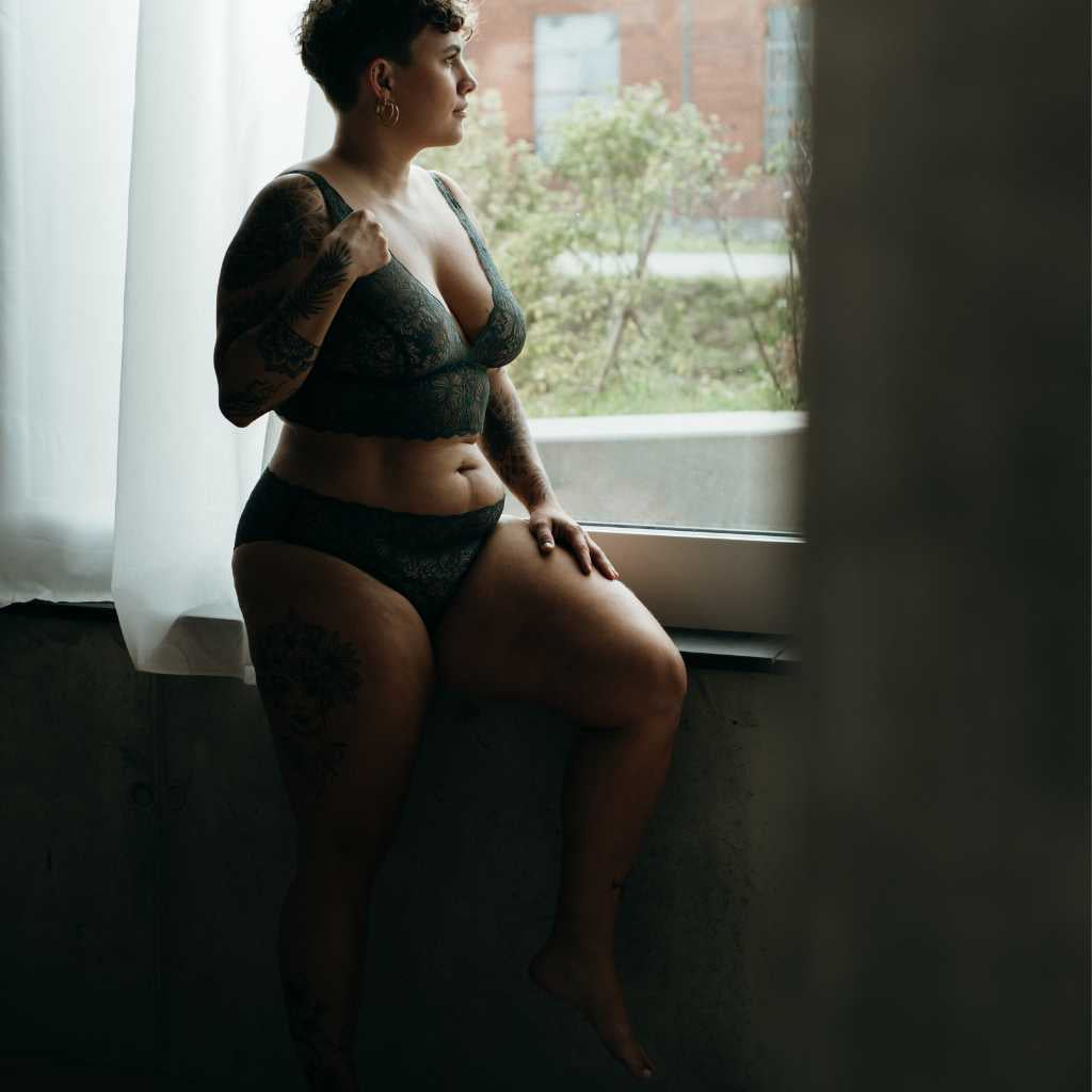 Woman at boudoir shoot wearing green lingerie and looking out the window.