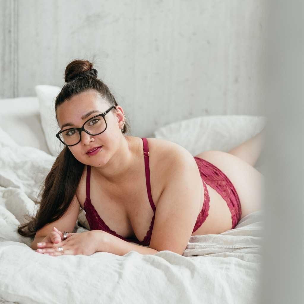 Self-love boudoir shoot - woman in bed wears red underwear and matching lipstick