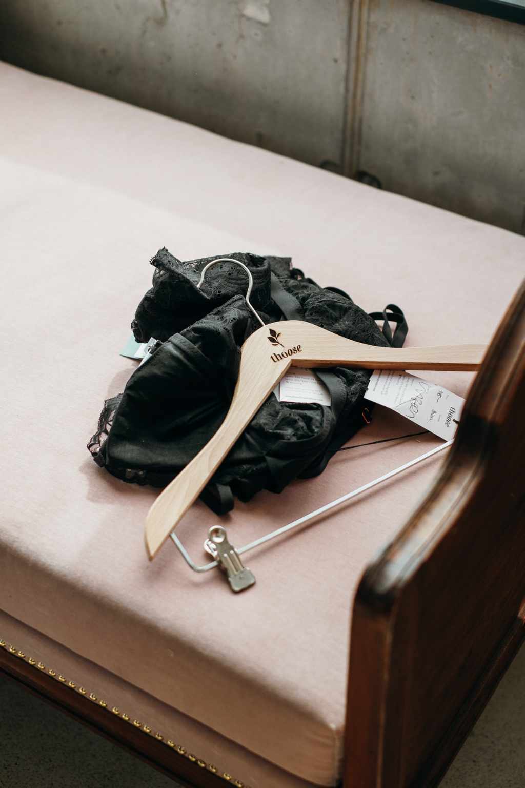 Black clothes and a coat hanger lie on a rose sofa.