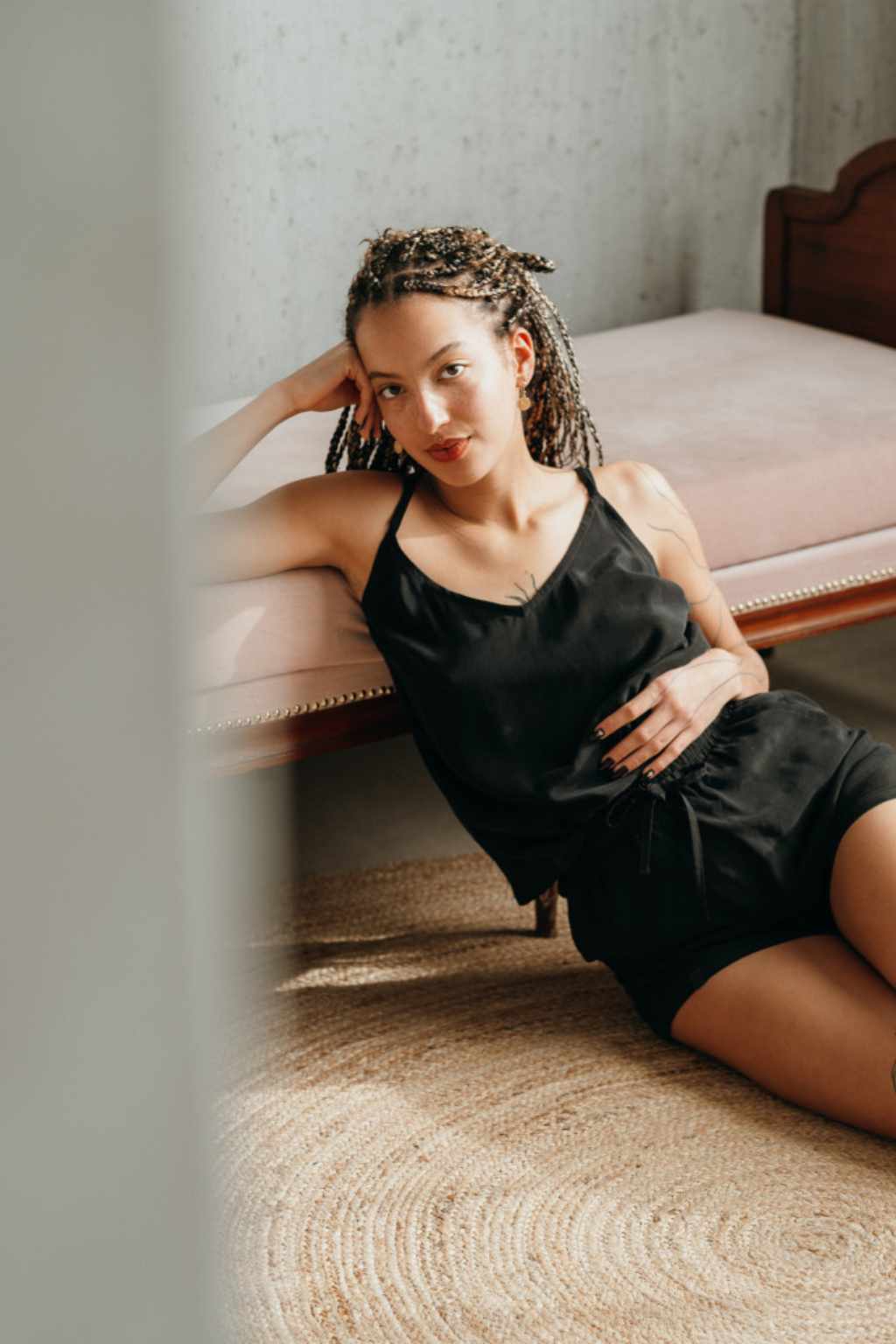 Model in short pyjamas made of cupro sits behind a column in front of the sofa.