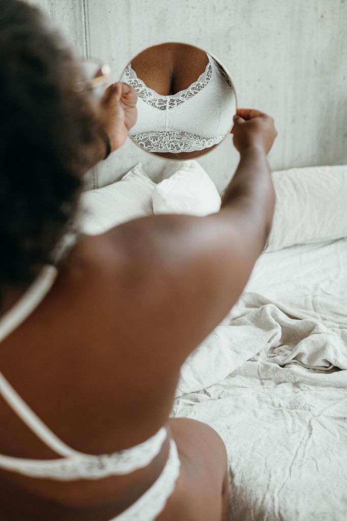 Woman in white padded lace bra looking at it in a small mirror