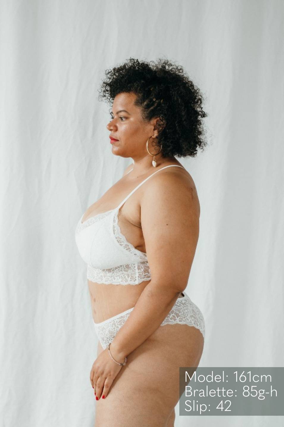 Model mit schwarzen Locken trägt Bralette Vivi in Grösse 85 G-H in weiss. 