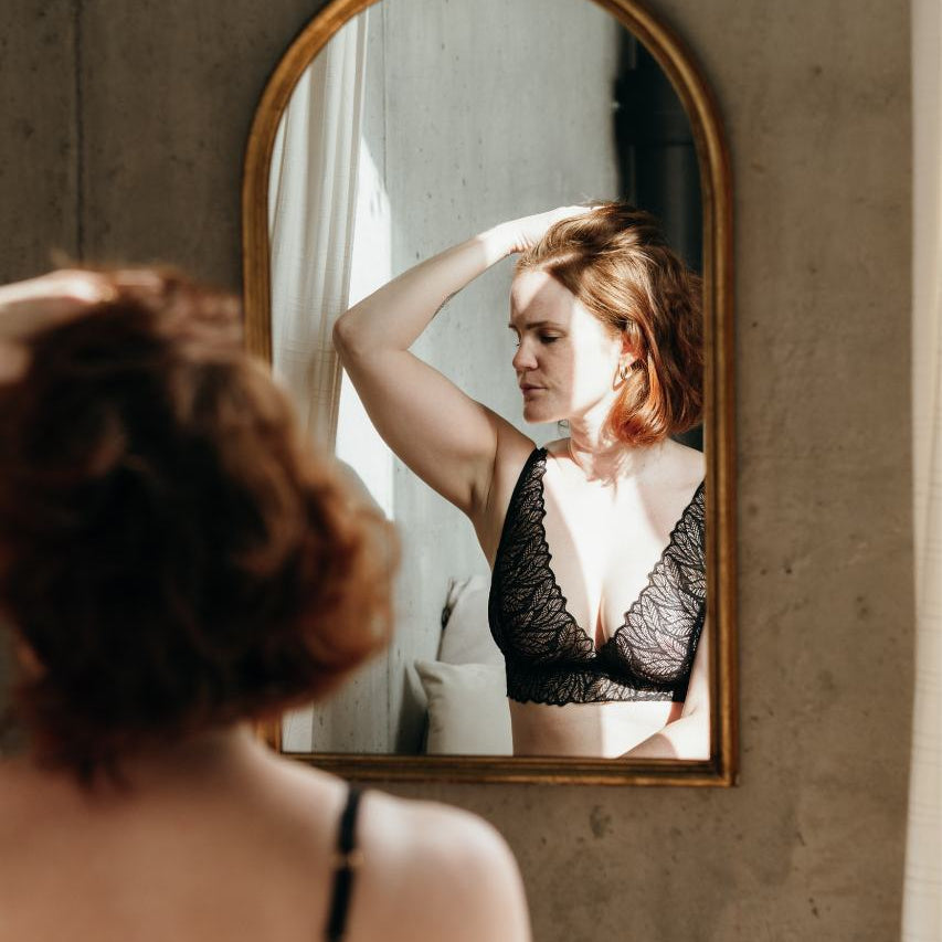 Boudoir photography - model in romantic lingerie looking at herself in the wall mirror.