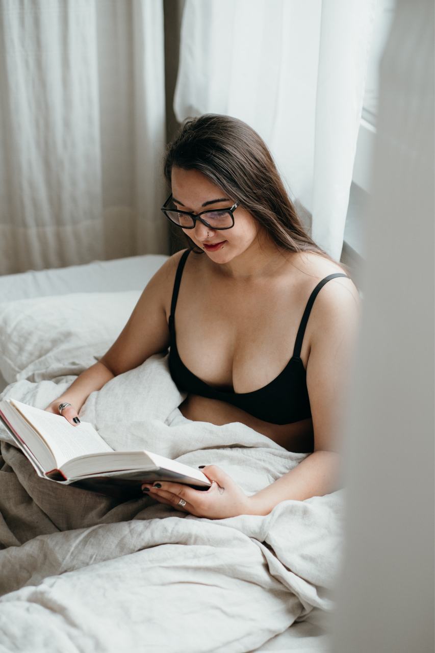 Boudoir photoshoot - woman in black bra sitting in bed and reading.