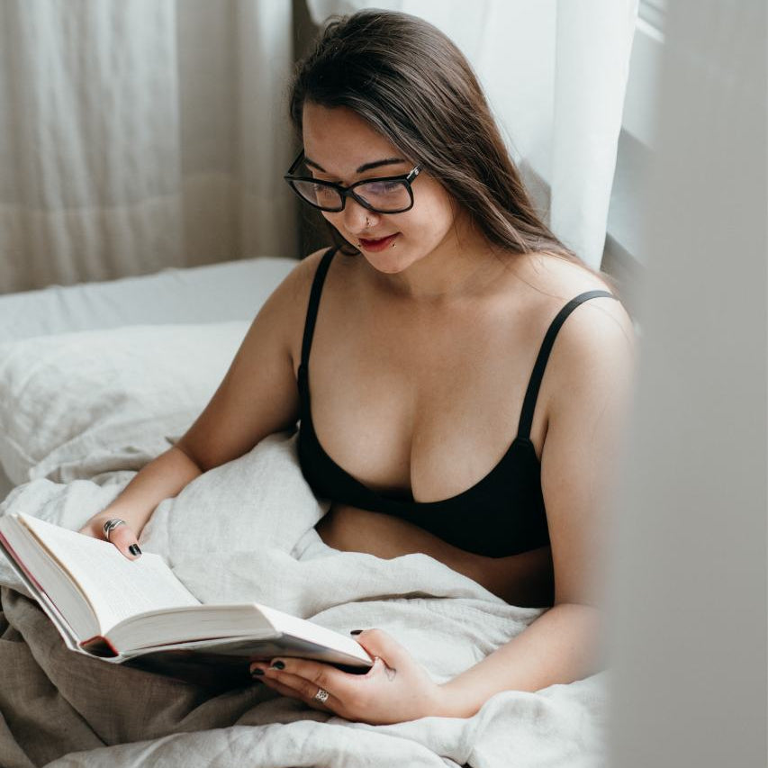 Boudoir photoshoot - woman in black bra sitting in bed and reading.