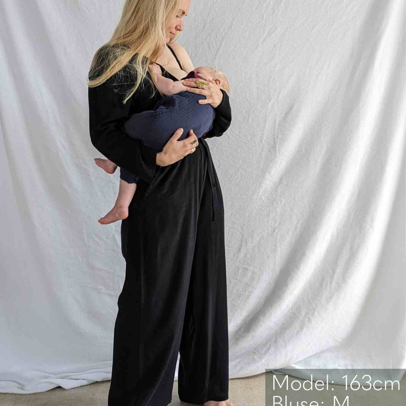 Woman in black blouse and culottes carries baby in her arms.