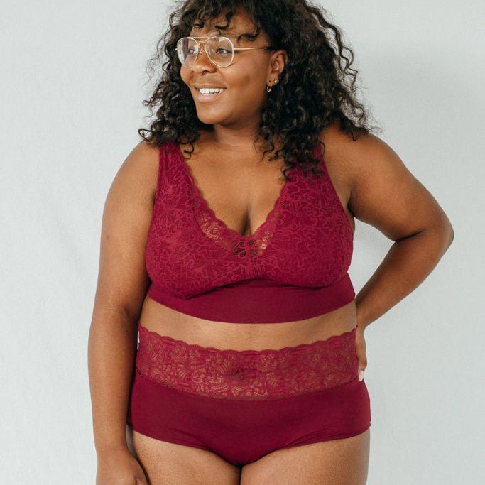 Stehende Frau trägt das Modell "Nelly" in Ruby rot mit einem Bralette und einem Höschen, dass sich weich um die Taille und Hüfte schmiegt