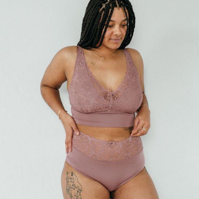Tattowierte Frau trägt schöne smokey rose Unterwäsche aus Slip und Bralette, welche die Brüste mit einem Jersey Unterbrustband hält.