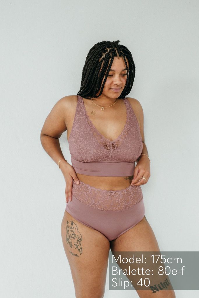 Tattowierte Frau trägt schöne smokey rose Unterwäsche aus Slip und Bralette, welche die Brüste mit einem Jersey Unterbrustband hält.