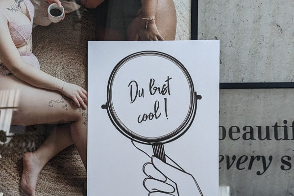 das Poster "du bist cool" vor einem Bild mit zwei Frauen in Unterwäsche