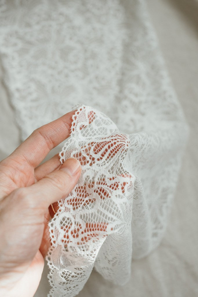 Hand hält weisse Spitze mit verspieltem Muster aus recycelten Fasern.