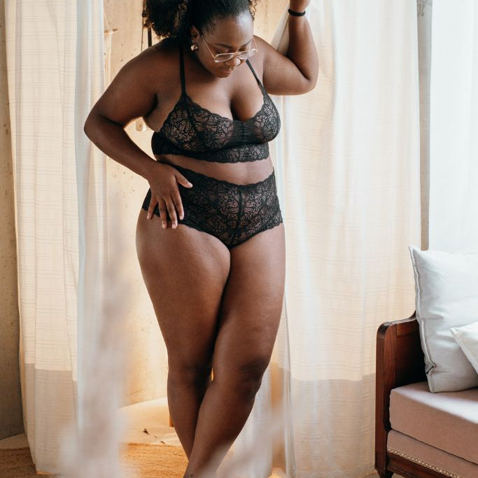the woman in the black underwear pulls aside the curtain and looks down at herself 