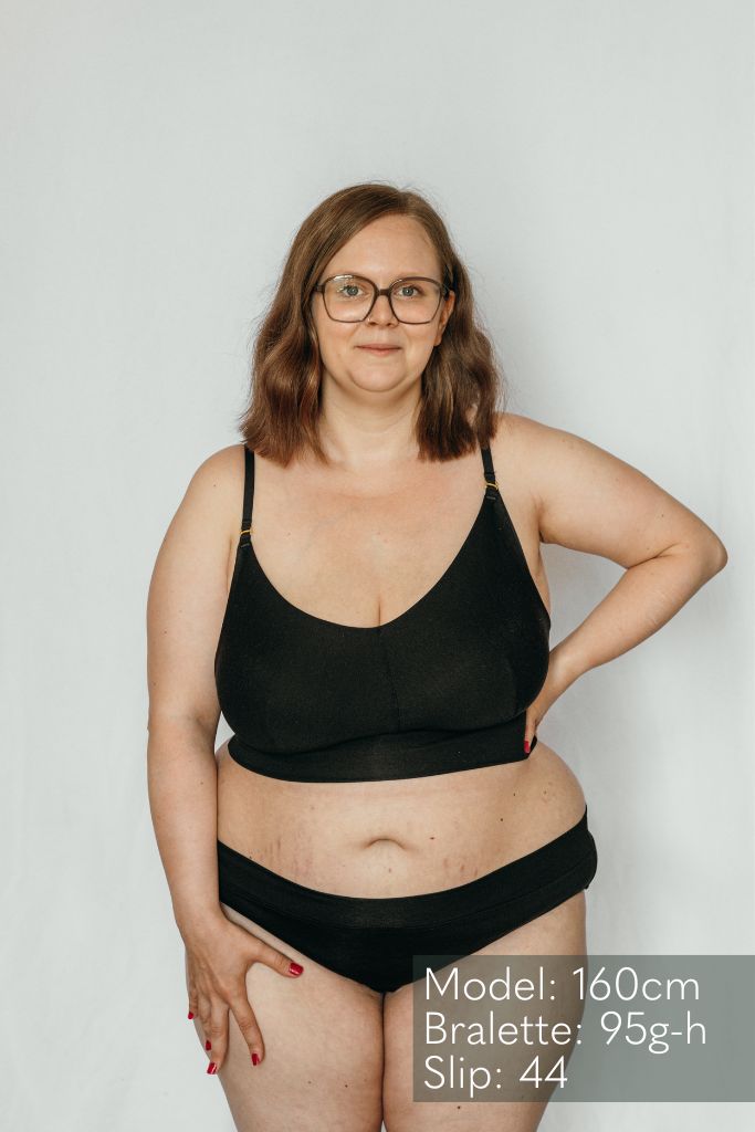 die Frau mit der Brille präsentiert das Emma Mama Bralette und den passenden Slip dazu in schwarz