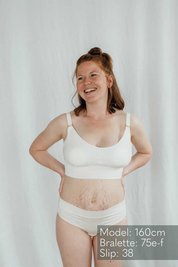 die lachende Frau präsentiert den Emma Mama Bralette und Slip in weiss
