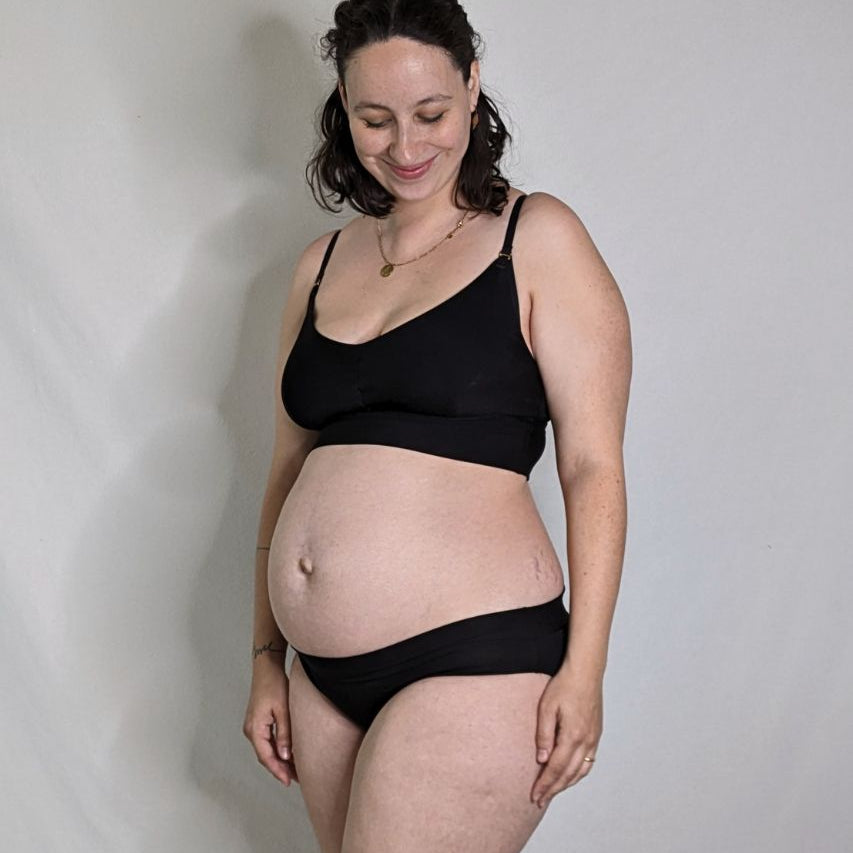 The pregnant woman is wearing the Emma panties and the Mama Emma Bralette in black