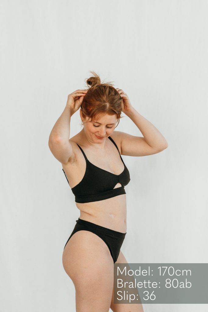 Das Model steht seitlich und trägt ein Oberteil und die cheeky Unterhose in schwarz