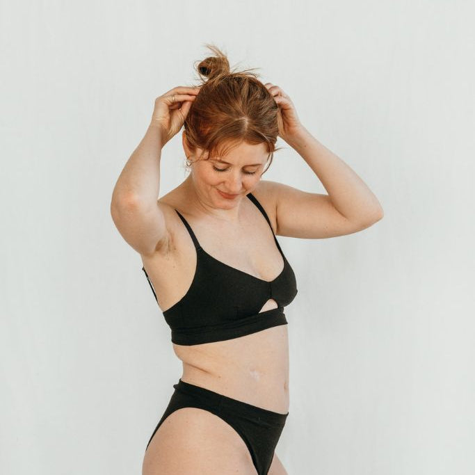 Das Model steht seitlich und trägt ein Oberteil und die cheeky Unterhose in schwarz