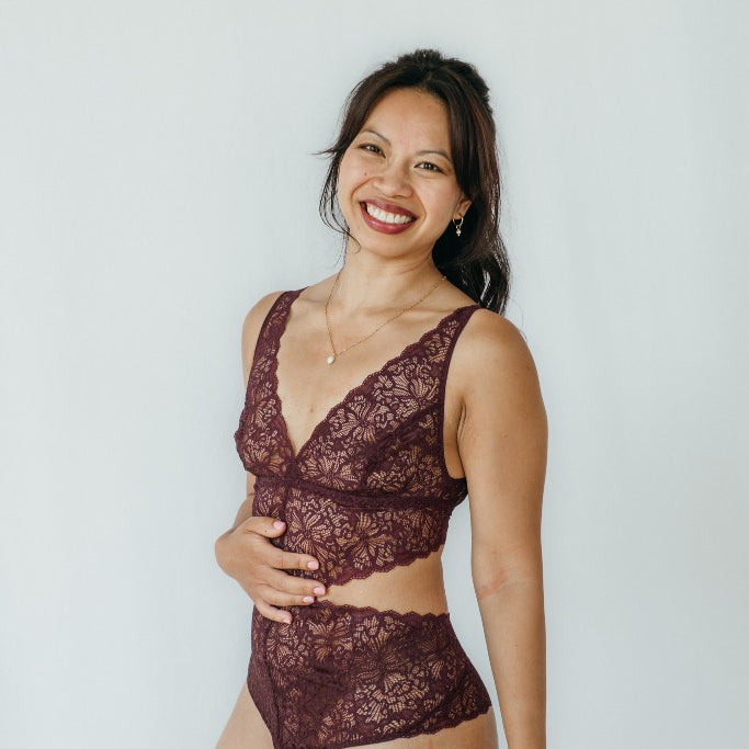 Model trägt Alison Body in der Farbe Aubergine. Sie steht leicht seitwärts und hält sich die Hand an den Bauch.