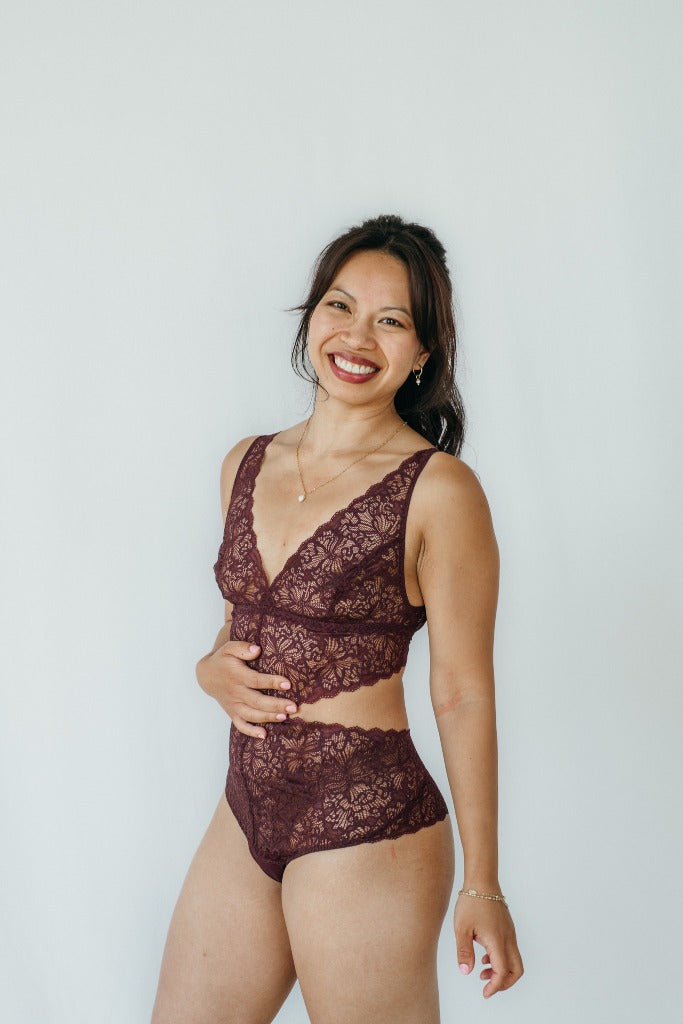 Model trägt Alison Body in der Farbe Aubergine. Sie steht leicht seitwärts und hält sich die Hand an den Bauch.