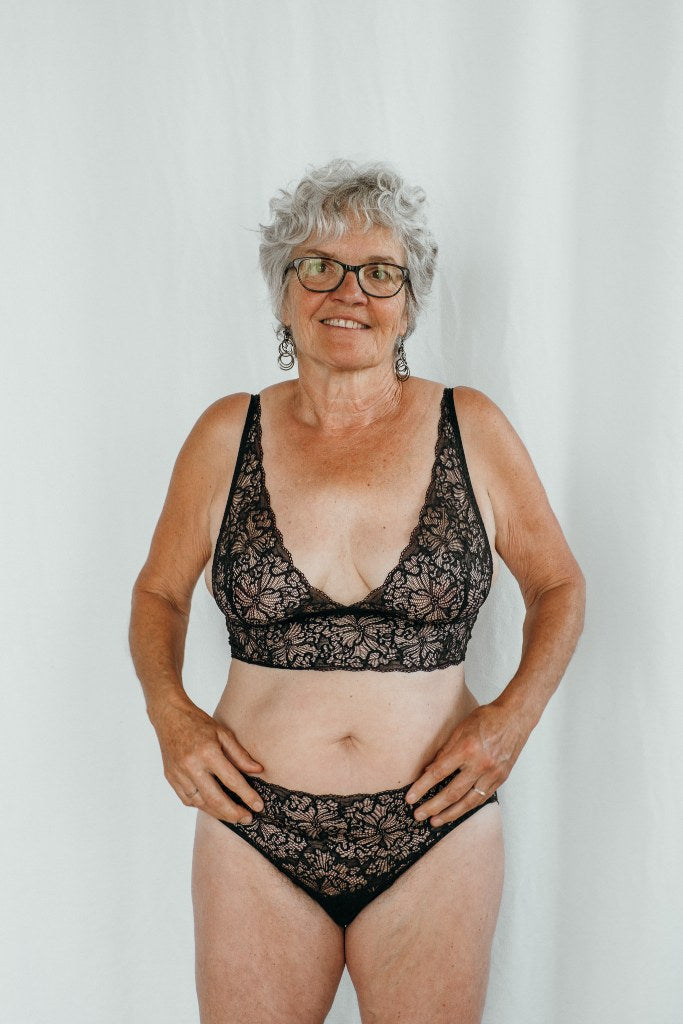 Donna in reggiseno e mutandine di pizzo nero in piedi davanti a uno sfondo bianco.