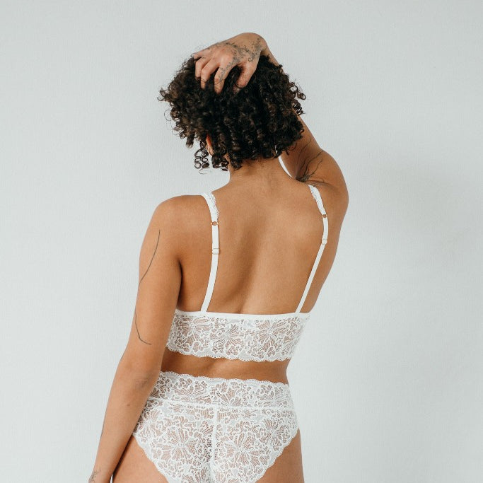 the woman is seen from behind and wears a lace dessou with adjustable straps