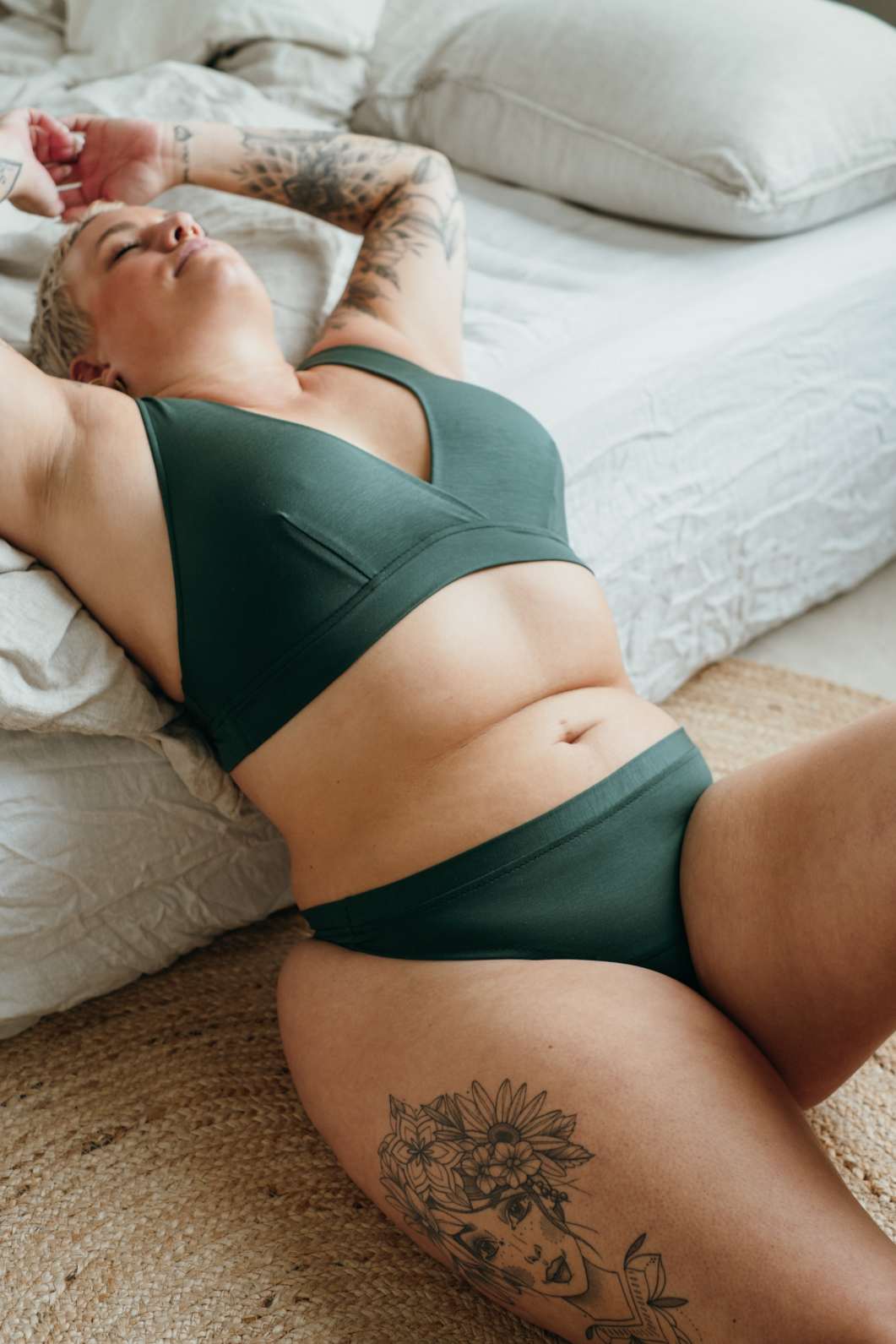 Model wears sustainable underwear, sits in front of the bed and leans over the edge.