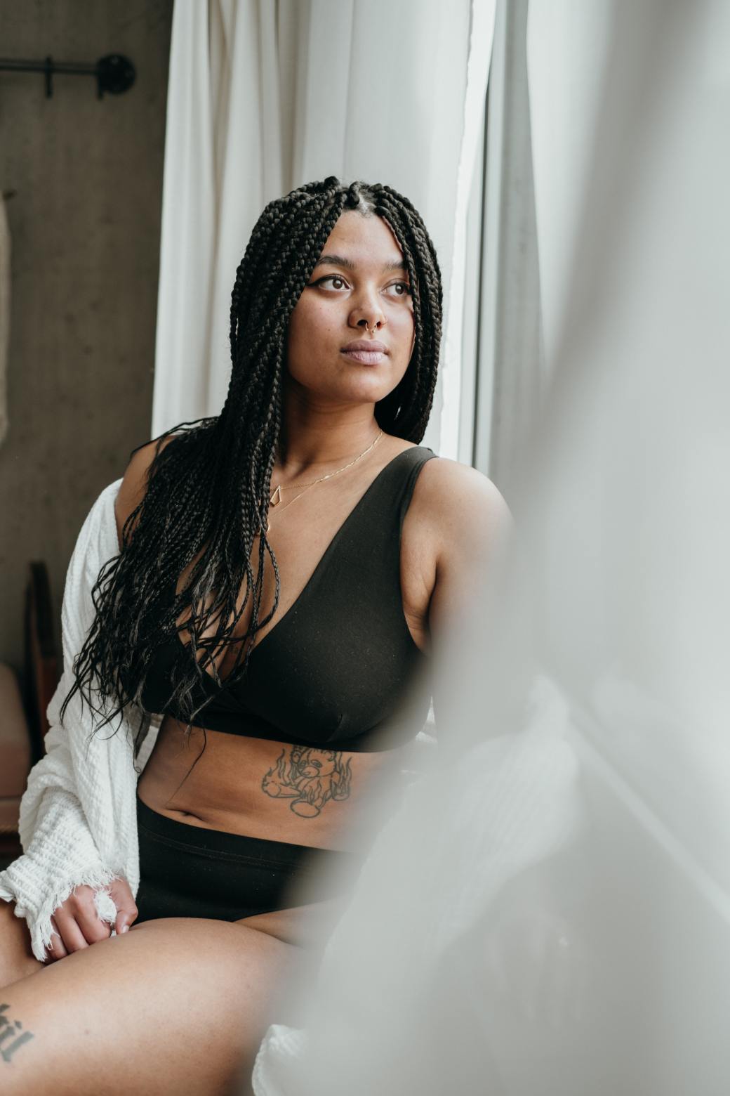 Romantic shot of model in black lingerie, with white blanket in front of the window.