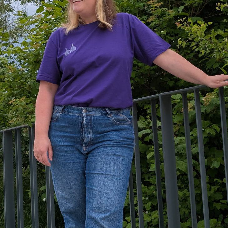 Foto zeigt Jess mit dem violetten Boobs Club Shirt von vorne. Sie lächelt seitwärts in die Kamera.