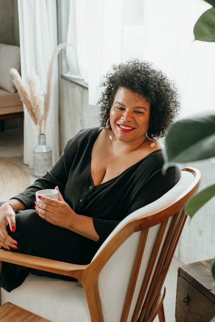 Woman sits in chair and drinks coffee.