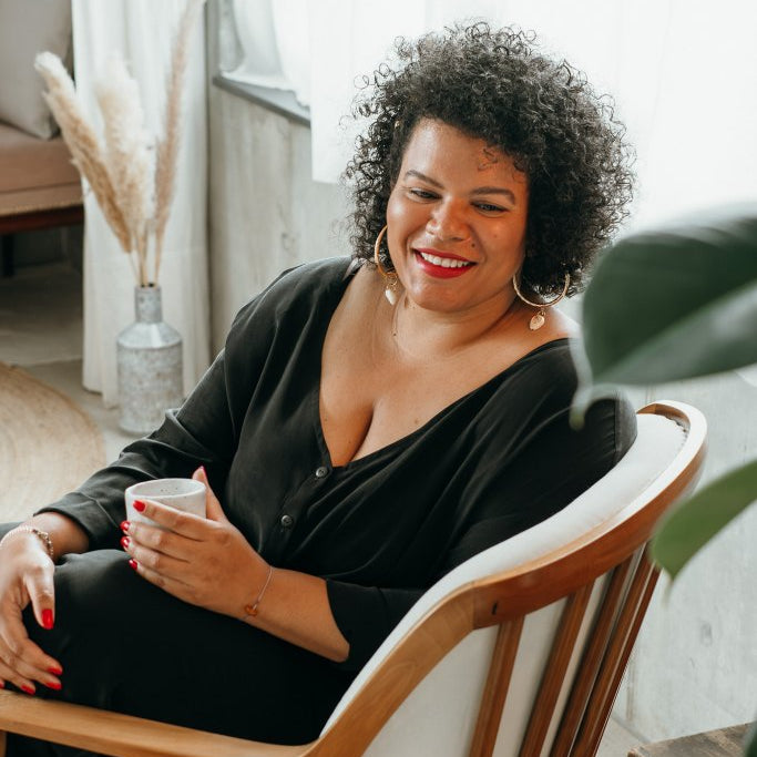 Woman sits in chair and drinks coffee.
