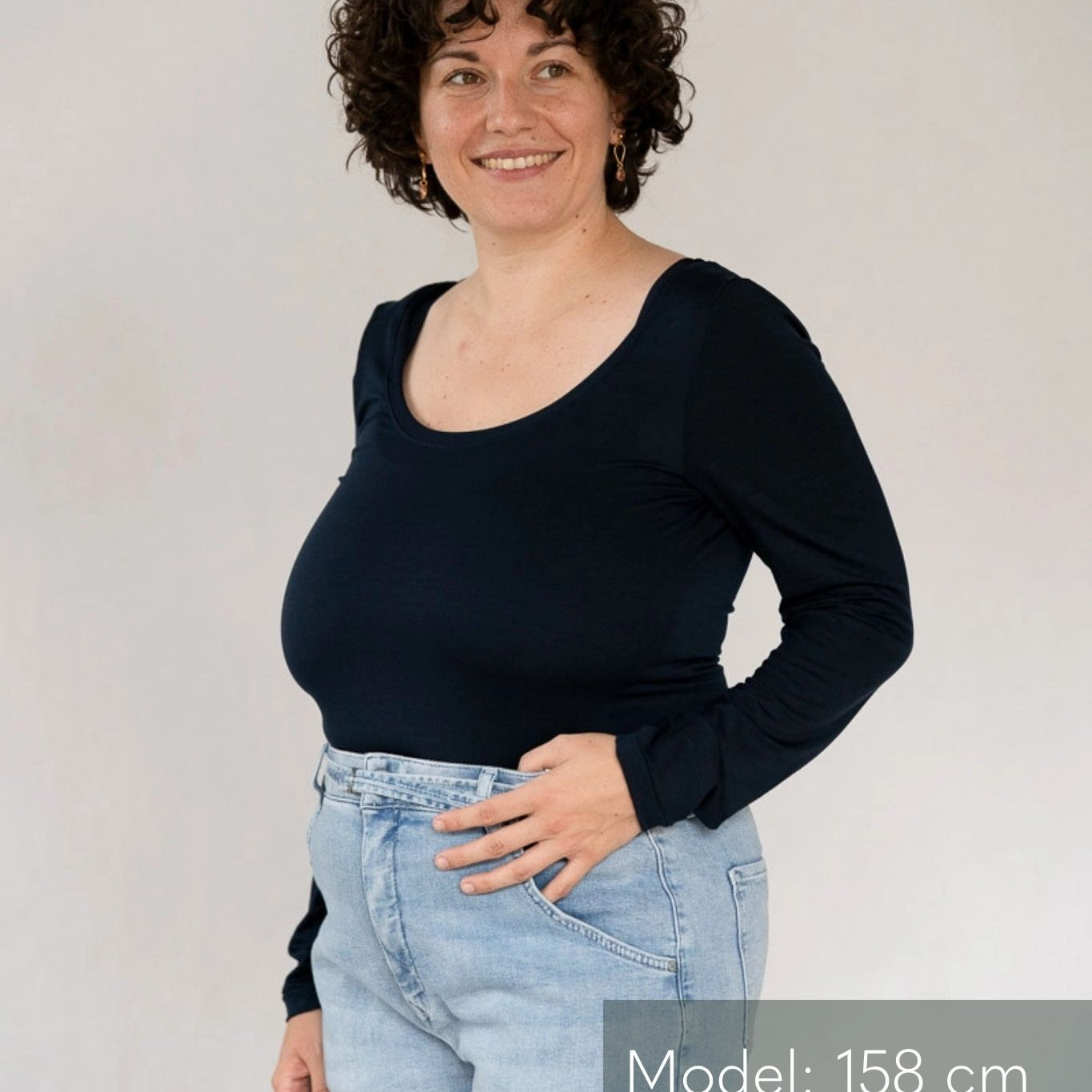 Model steht vor weissem Hintergrund, eine Hand lässig in die Jeans gehakt. Sie trägt dazu das Dolly Longsleeve in Night Blue.
