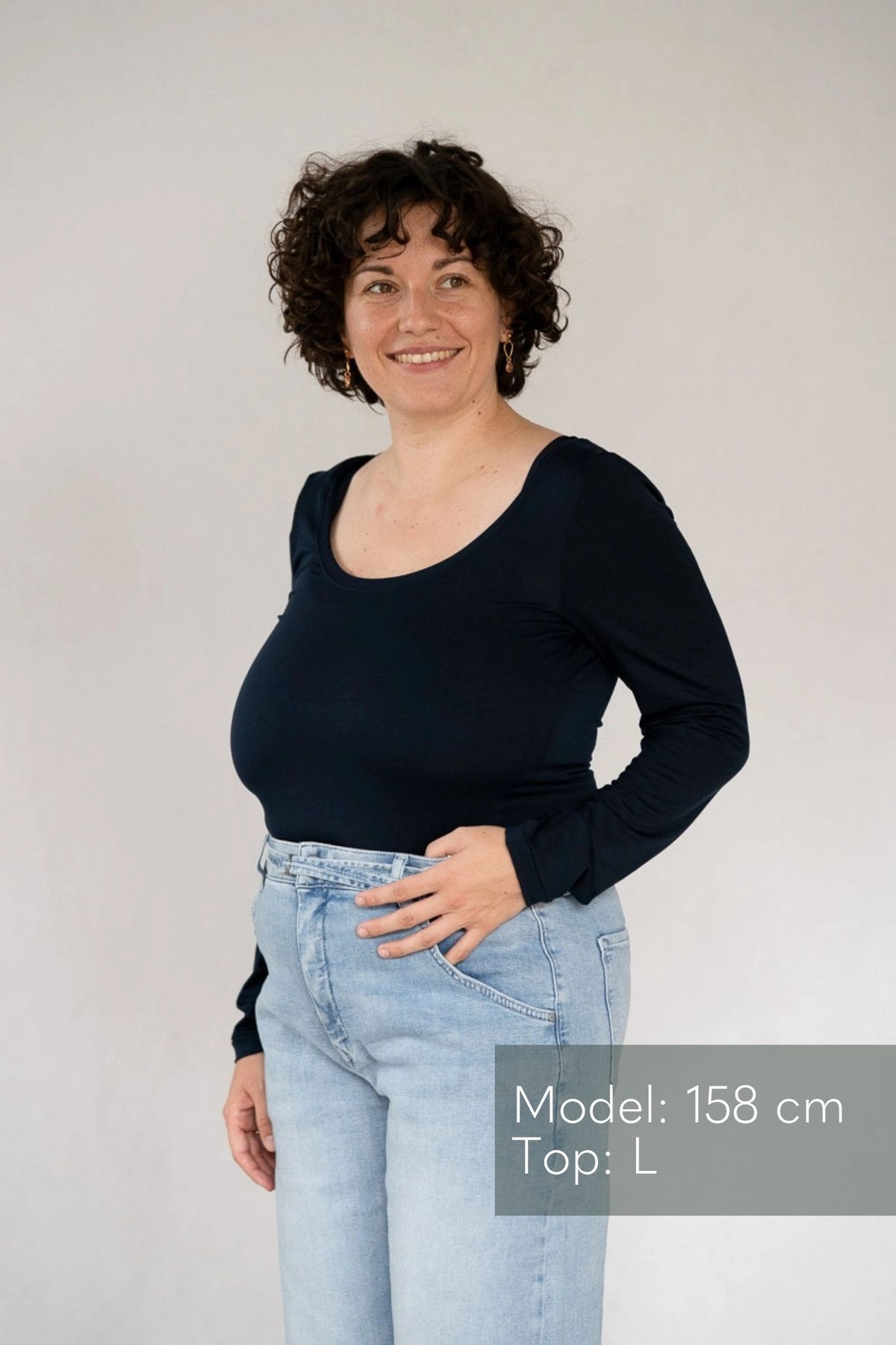 Model steht vor weissem Hintergrund, eine Hand lässig in die Jeans gehakt. Sie trägt dazu das Dolly Longsleeve in Night Blue.