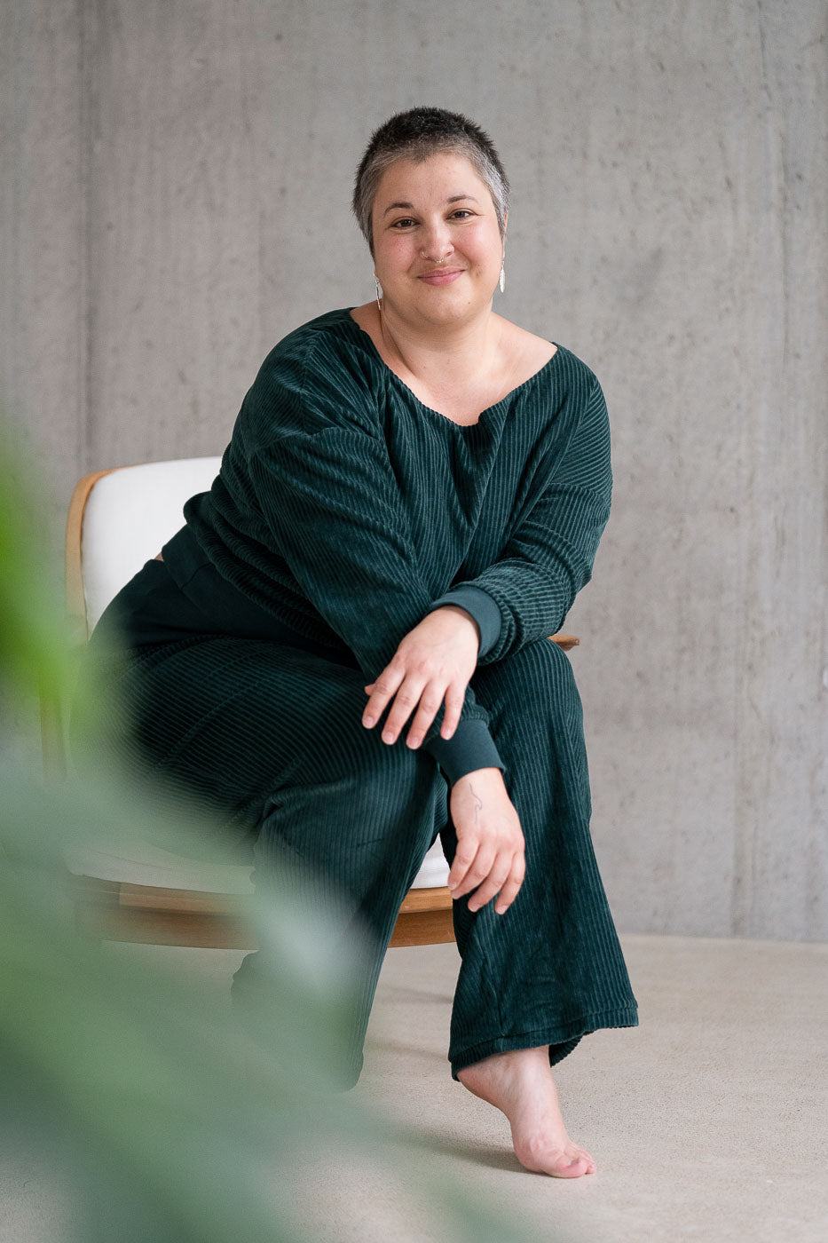 Model sitzt im jadegrünen Pyjama auf dem Sessel und lächelt direkt in die Kamera