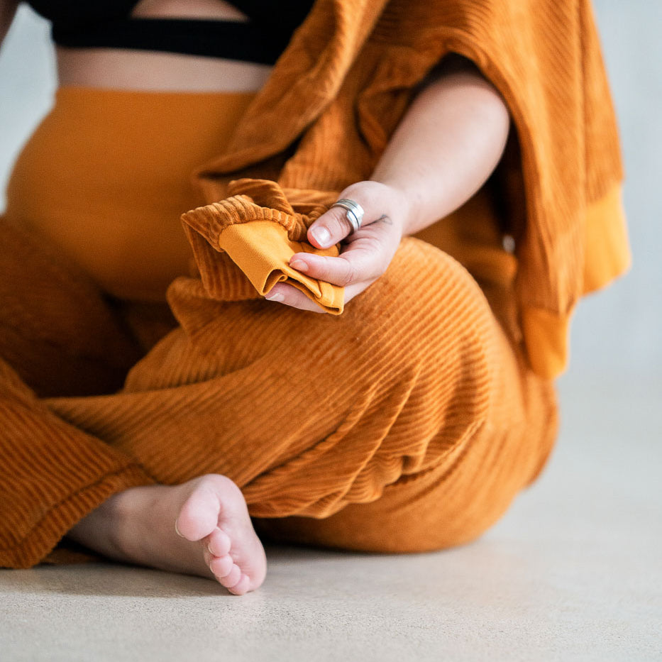 Model sitzt im ockerfarbigen Pyjama auf dem Boden im Schneidersitz.