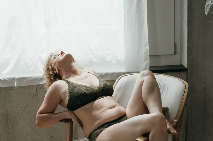 Model trägt das Gisele Set in Olive und sitzt auf einem weissen Sessel. Den Rücken streckt sie über eine Armlehne.