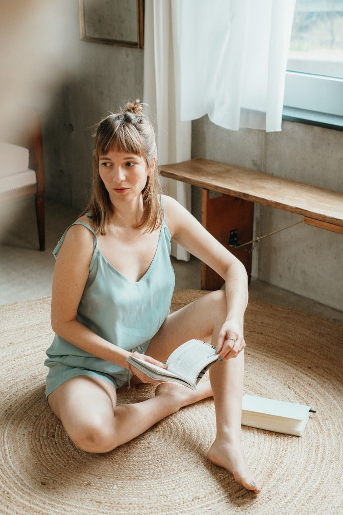 The woman holds a book in her hand and shows herself in the Kat top in the color summer mint