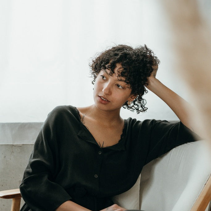 La modella si siede sulla sedia e indossa un bellissimo abito nero.
