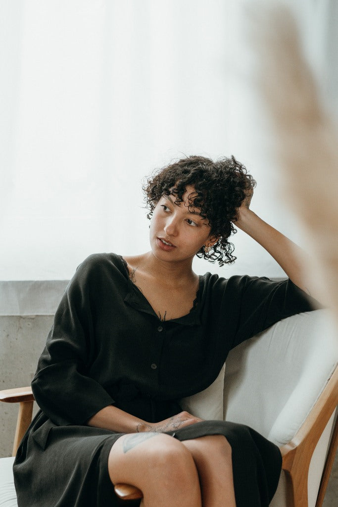 La modella si siede sulla sedia e indossa un bellissimo abito nero.