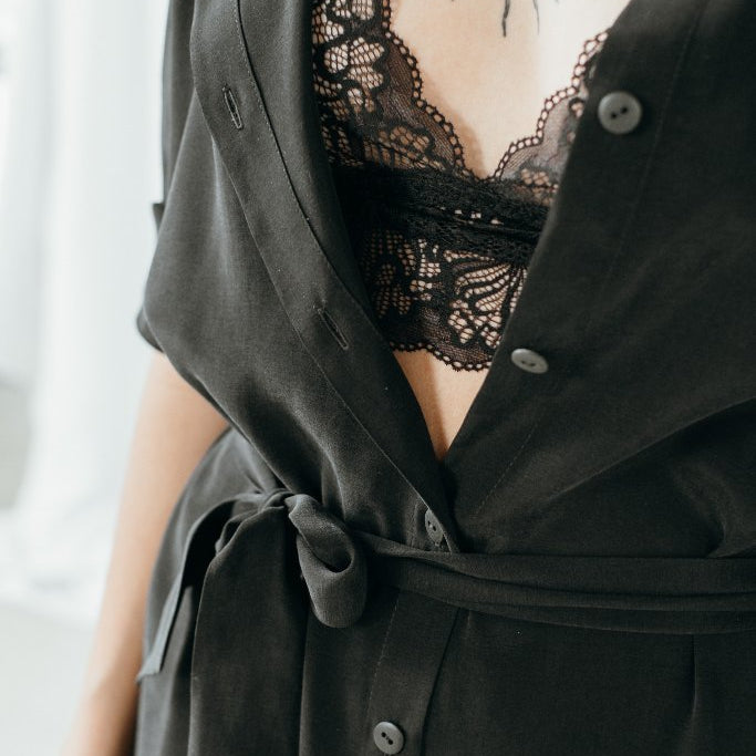 Bralette La modella indossa un abito nero e sotto di esso fa capolino un pizzo nero.