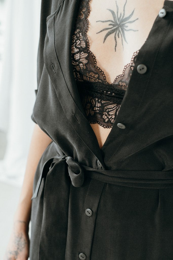 Bralette La modella indossa un abito nero e sotto di esso fa capolino un pizzo nero.