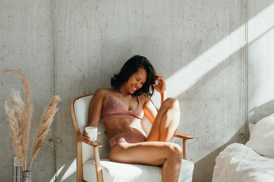 das Model sitzt auf dem Stuhl mit angewinkeltem Bein und trägt dabei schöne Lingerie mit gutem Support