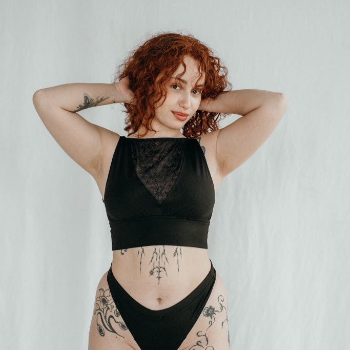 la modella tiene le braccia vicino alla testa e indossa slip neri con un top in pizzo e jersey nero