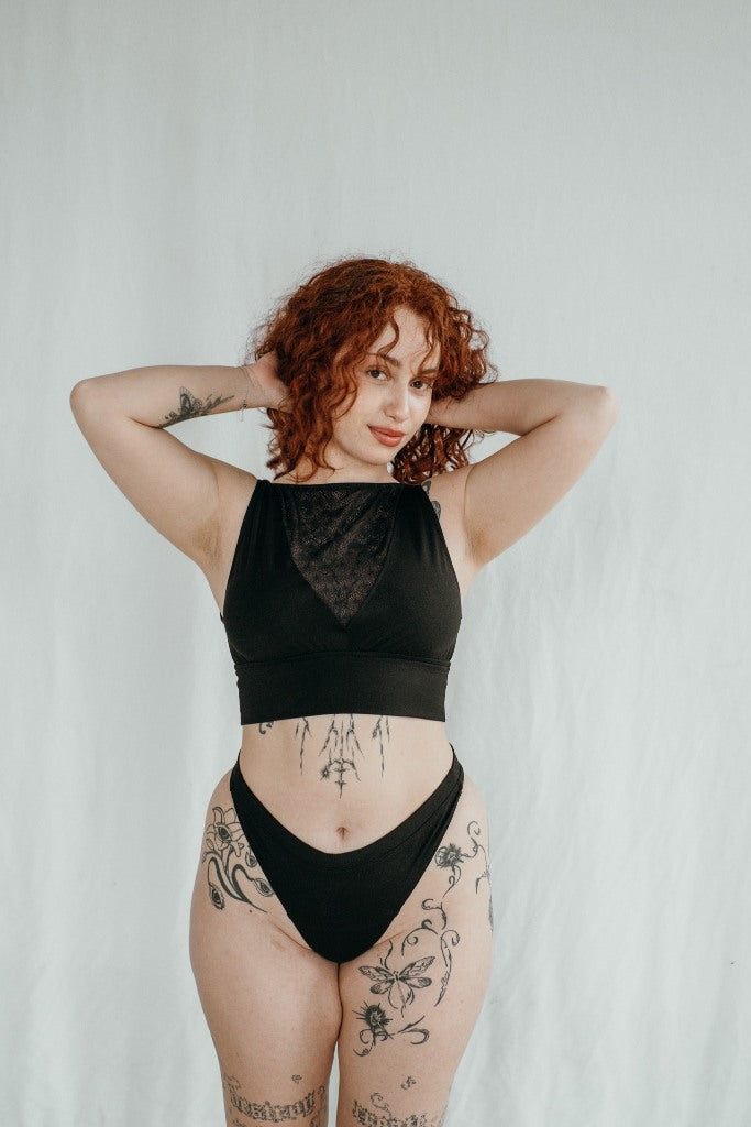 la modella tiene le braccia vicino alla testa e indossa slip neri con un top in pizzo e jersey nero