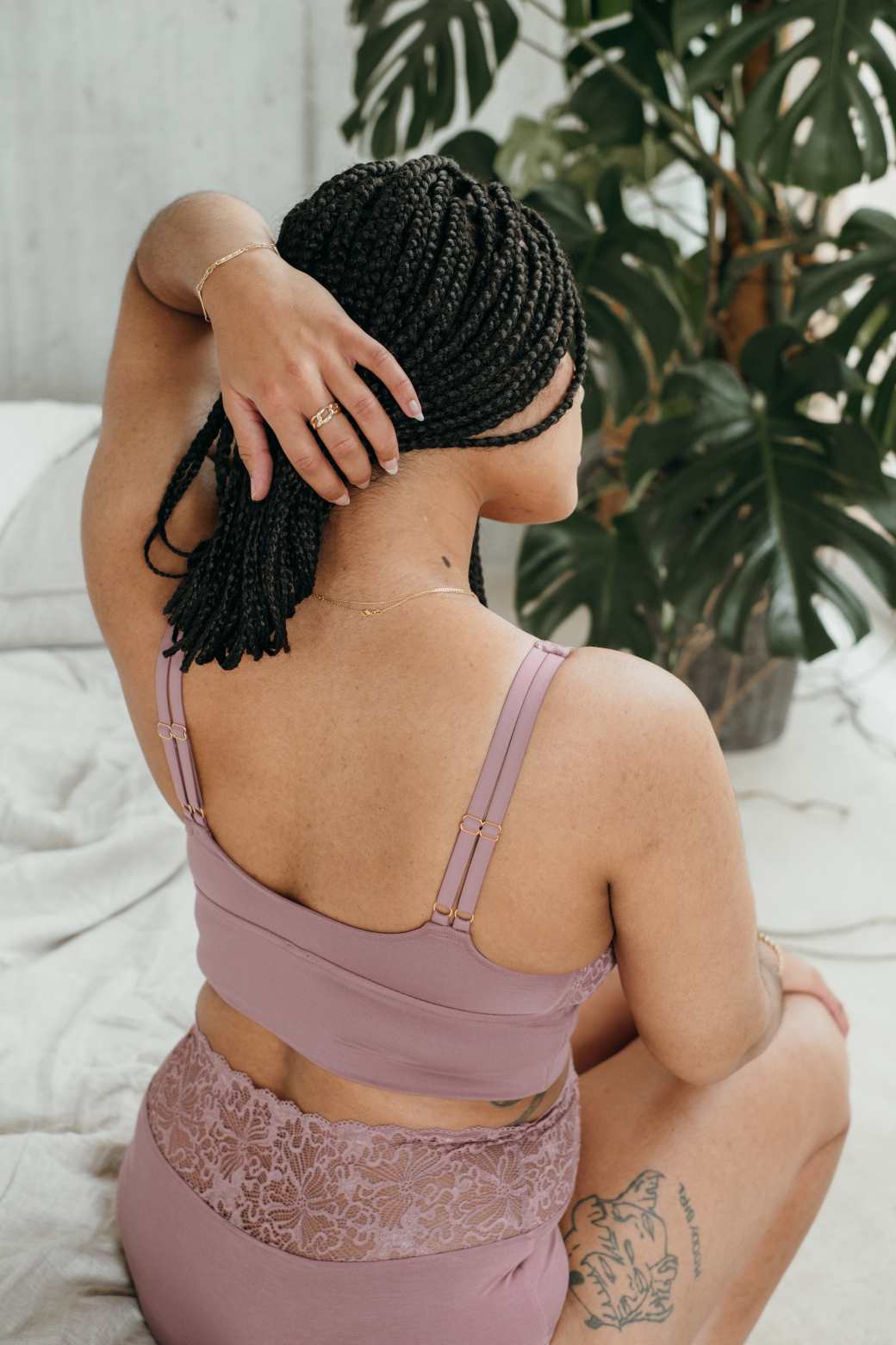 Model in Unterwäsche in Altrosa sitzt auf dem Bett uns streicht die Haare zur Seite.