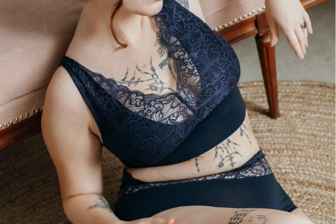 die Frau sitzt auf dem Boden und lehnt sich an. dabei trägt sie Unterwäsche in der Farbe night blue mit doppelten Trägern