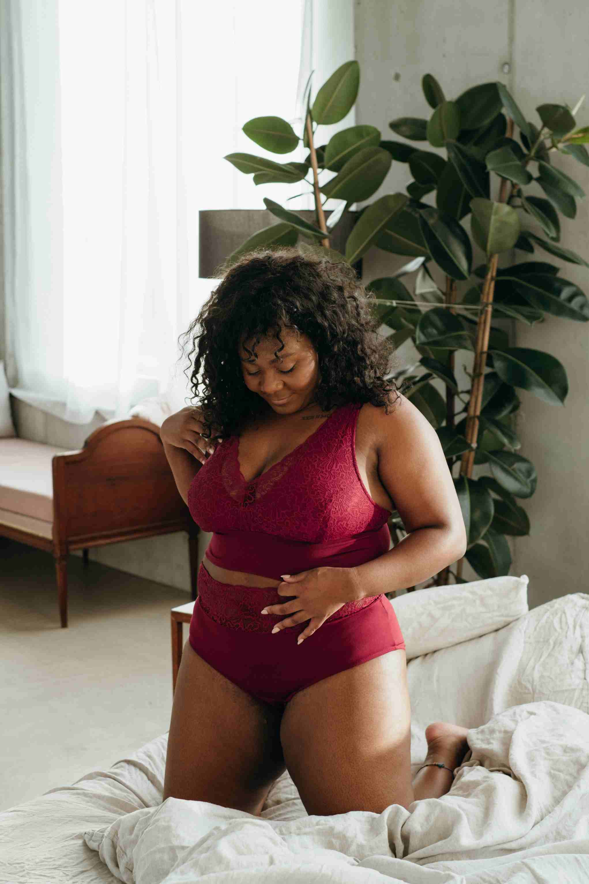 Model in red bra with good support and matching underpants kneeling on bed.